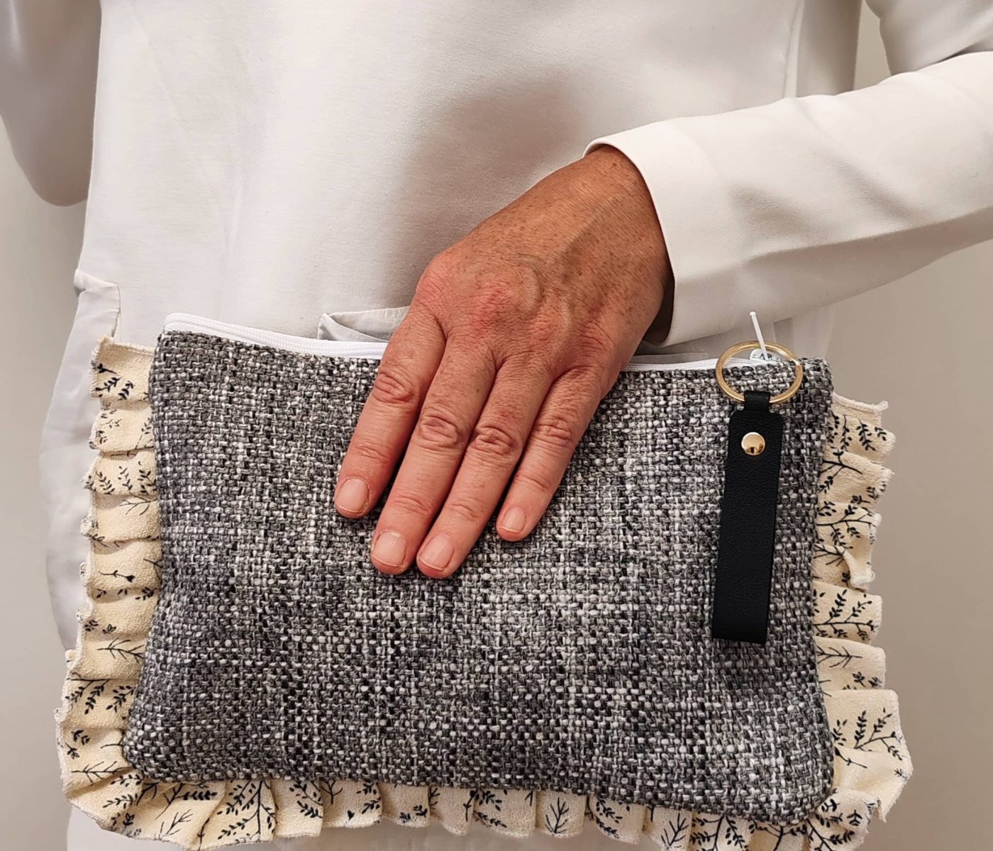 Bolso de mano hecho a mano con tela de tapicería gris y volante de algodón estampado en tonos claros, sostenido por una mano